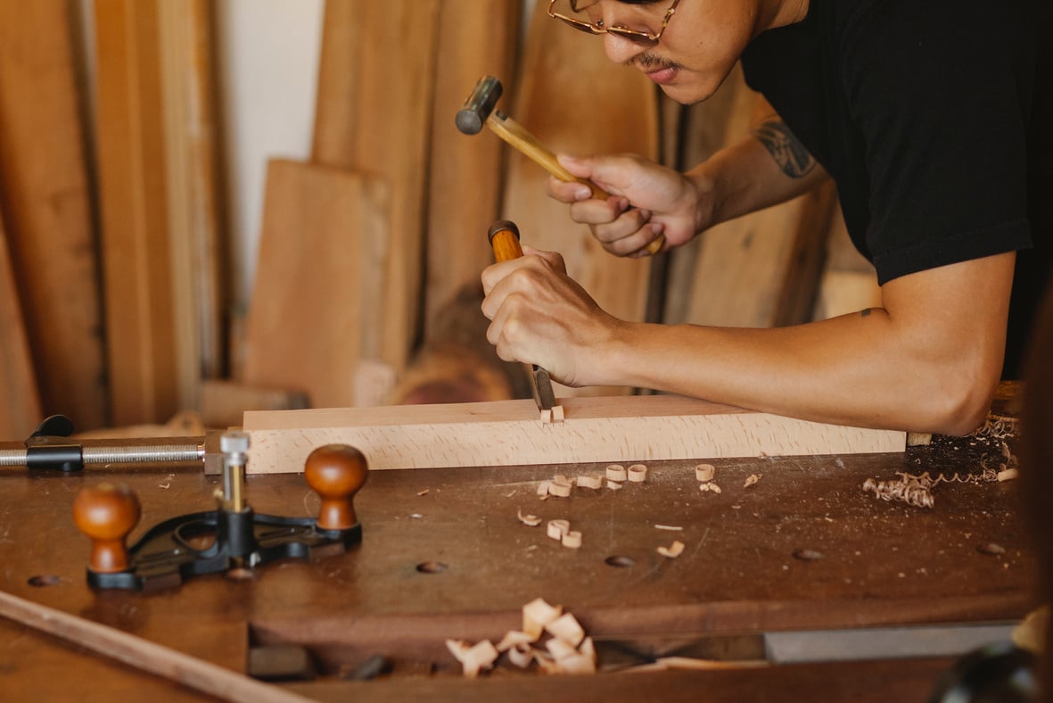 Focused artisan making hole on plank with hammer and chisel